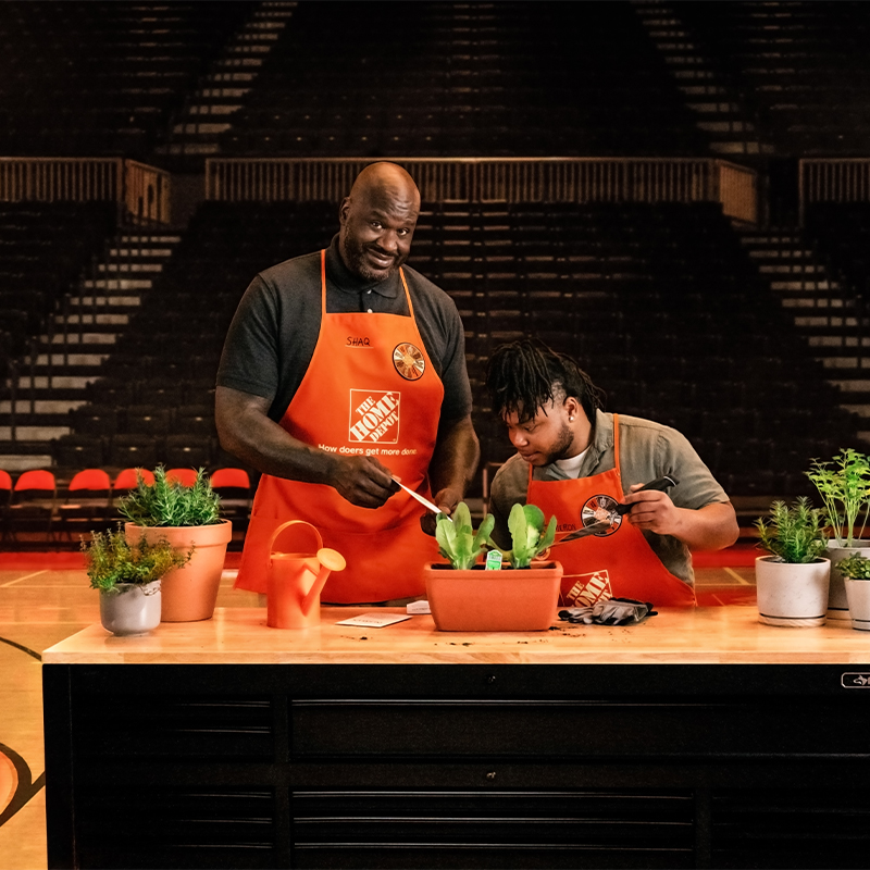 Shaq and HD employee at a table with plants on a basketball court